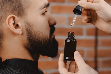 Barber applies beard oil with dropper for man in barbarshop.