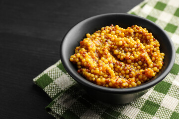Whole grain mustard in bowl on black wooden table, closeup. Space for text