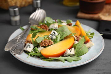 Tasty salad with persimmon, blue cheese and walnuts served on grey wooden table, closeup