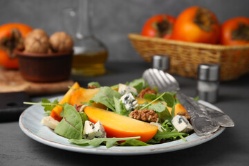 Tasty salad with persimmon, blue cheese and walnuts served on grey wooden table, closeup