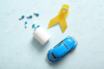 Golden ribbon with pills and toy car on light blue background. Children cancer awareness concept
