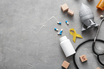 Golden ribbon with stethoscope, pills and toys on grey grunge background. Children cancer awareness concept