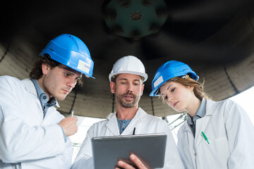 workers looking at a tablet pc underneath a turbine