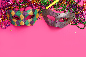 Shiny carnival masks with party horn and decor for Mardi Gras celebration on pink background
