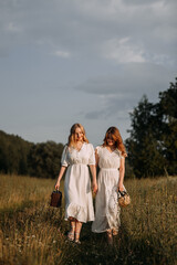 The image features two women wearing white dresses standing outdoors in a field. 5620