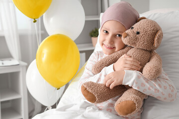 Little girl after chemotherapy with toy bear lying in bed at hospital. International Childhood Cancer Day - obrazy, fototapety, plakaty