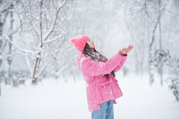 Beautiful teenage girl 14-15 year old wearing pink winter jacket and knitted hat play with snow and...