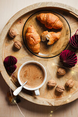 Cup of coffee, chocolate croissants on a wooden tray with Christmas decorations.