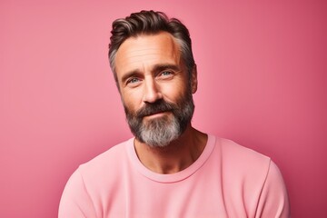 Portrait of a handsome mature man with beard and mustache looking at camera against pink background