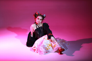 Young woman in colored dress and black jacket sitting on the floor on pink background