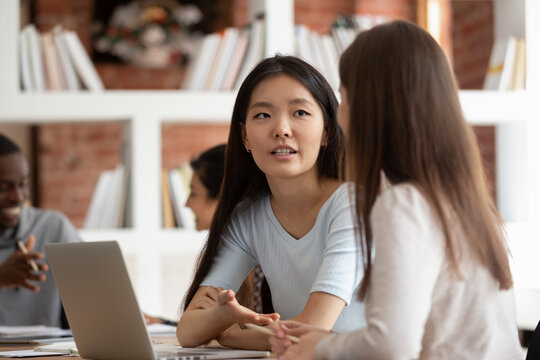 Millennial Asian female talk brainstorming with teammate work on shared school project together, multiracial girl students speak chat cooperating studying discussing or sharing ideas at lesson