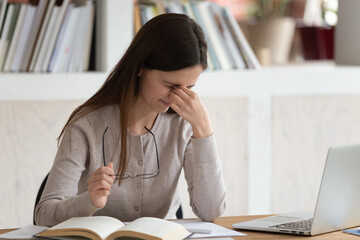 Tired female student sit at desk working at laptop massage rub eyes suffering from blurry vision or...