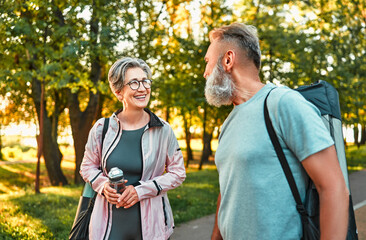 Preparation for morning training in the fresh air. Healthy lifestyle. Support of a healthy body and joints. Couple of modern seniors talking before jogging, training.