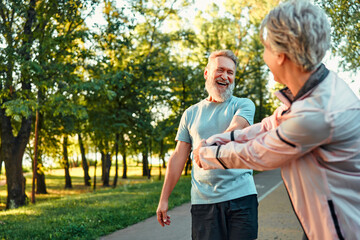 Happy couple outdoors in the park before a morning jog. An adult woman jokingly pulls her friend to...