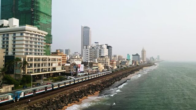 Aerial Colombo skyline with ocean, train and city traffic. Sri Lanka capital landscape, coastal urban view. Travel, real estate, commercial, cinematic use of tropical metropolis.