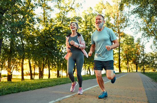 Happy and healthy lifestyles. Caucasian aged people with sincere smile on faces enjoying outdoors cardio at green park. Active male and female pensioners in sport outfits spending time for workout.