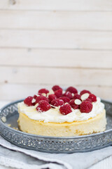 Classic New York cheesecake with whipped cream on top and fresh raspberries on white wooden background close up selective focus