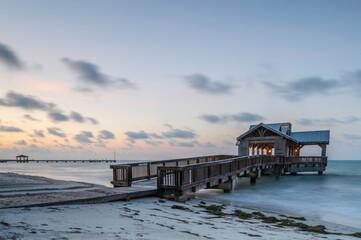 A wooden pier or jetty, reaching out into a calm ocean, at sunrise, as colour creeps into the sky.