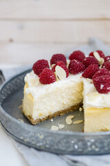 Classic New York cheesecake with whipped cream on top and fresh raspberries on white wooden background close up selective focus