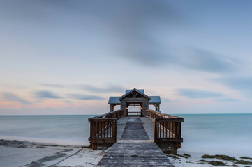 A wooden pier or jetty, reaching out into a calm ocean, at sunrise, as colour creeps into the sky.