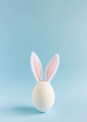 an egg with bunny ears in the center of light blue background Easter card concept 