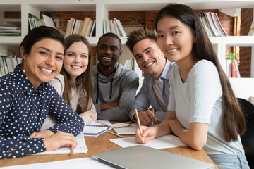 Smiling multiethnic students sit at desk working studying in classroom posing for group picture together, portrait of positive motivated multiracial young people teammates cooperating at lesson