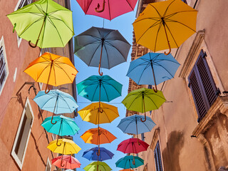 Fototapeta na wymiar Colorful umbrellas hanging in a street of Novigrad, a charming town in Istria. Croatia, Europe