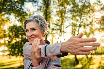 Active workout outdoors. Close up of pleasant grey haired woman in sportswear doing stretching...