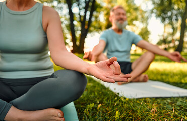 Relaxation of body and mind. Close up of aged woman and man sitting in lotus position on yoga mats...