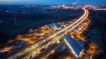 Fototapeta na wymiar This aerial image captures the bustling E19 highway as it courses near Halle, Brussels, during evening rush hour. The scene is alive with the glow of headlights and tail lights, illuminating the