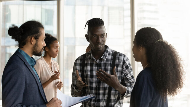 Business opportunity. Young biracial salesman explain commercial contract benefits to potential customers on informal meeting. Group of diverse workmates discuss good sales statistics in paper report