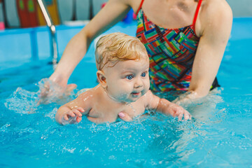 Fototapeta na wymiar Teaching a newborn boy to swim in a pool with a coach. Baby swimming courses. The child swims in the pool