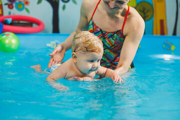 Obraz na płótnie Canvas Teaching a newborn boy to swim in a pool with a coach. Baby swimming courses. The child swims in the pool