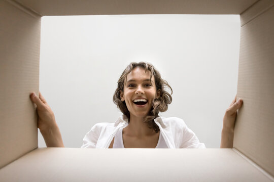 Excited happy young woman looking inside cardboard box with surprise, joy, amazement, unpacking paper container from shipment service, post office, getting parcel, purchase