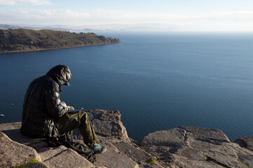 Unrecognizable man sitting on rocks overlooking Lake Titicaca