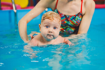Fototapeta na wymiar Baby swimming in the pool. Teaching a newborn boy to swim in a pool with a coach