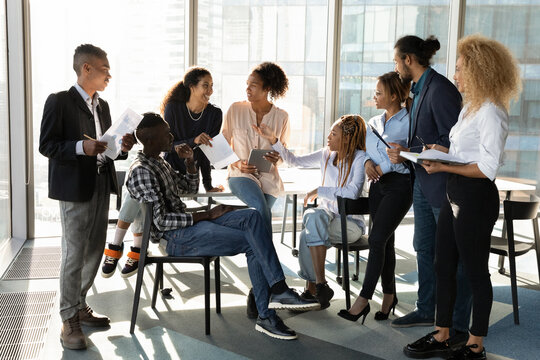 Young diverse ethnic business team and female leader talk chat at office space relax at break share ideas on project in work. Multiethnic staff members engaged in workshop training exchange opinions