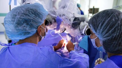 Rear view of cooperating two doctors looking at binoculars of microscope. Male neurosurgeon using the device carefully. - Powered by Adobe