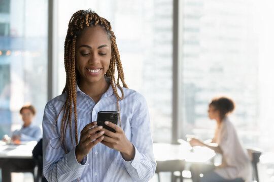 Modern tech in office. Smiling biracial female manager employee use phone at work text message to client colleague. Happy young lady worker read email document online on cell screen in app. Copy space