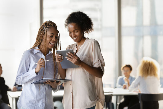 Happy young afro american females teammates enjoy solving business problem together using online and paper reports. Two millennial women employees feel glad to find perfect decision working together - Powered by Adobe