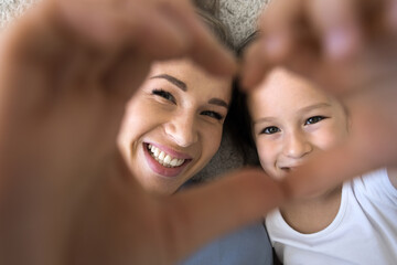 Fototapeta premium Close up shot daughter and loving mom showing symbol of affection, join fingers together look at camera through heart sign, feeling unconditional love, express support. Family ties, happy Mothers Day