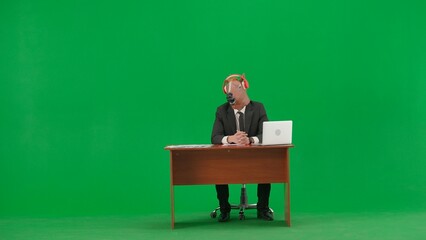 Man in business suit with horse head mask on studio green background. Businessman sitting at desk, listening to music with big red headphones. Concept of heavy office work.