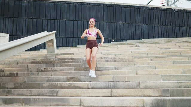 Sportswoman running down stairs during training. Slow motion of a young fit female in sportswear and headband jogging down stairs in city during outdoor fitness workout