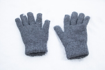 A pair of gray gloves laying on top of snow
