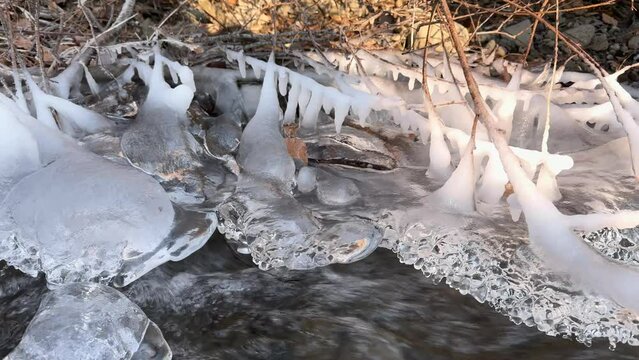The clear water of a mountain stream in the European Alps has frozen in the morning frost into artistic icicles, the fast flow is murmuring musically