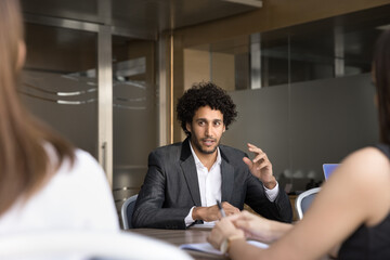 Positive young Arab business professional man talking to team of HR managers on job interview,...