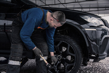 Fototapeta na wymiar Mechanic at a service station in overalls repairs a wheel on a car.
