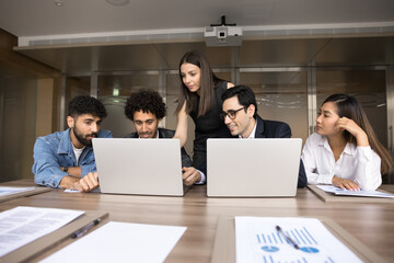 Obraz premium Focused diverse managers and young female business leader meeting at laptops together, watching video presentation on computers, working on startup, brainstorming on online project