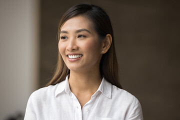 Cheerful young Asian professional woman casual portrait. Positive beautiful businesswoman, female employee posing indoors in office, looking away with beautiful toothy smile