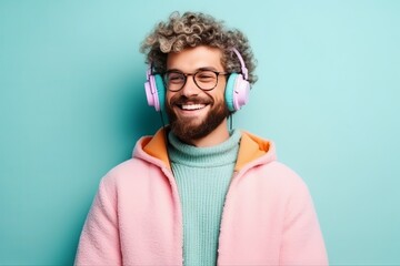Happy millennial man with beard enjoying music on headphones on a plain pastel background. Concept: audio podcasts and listening to books, self-education through stereo - obrazy, fototapety, plakaty